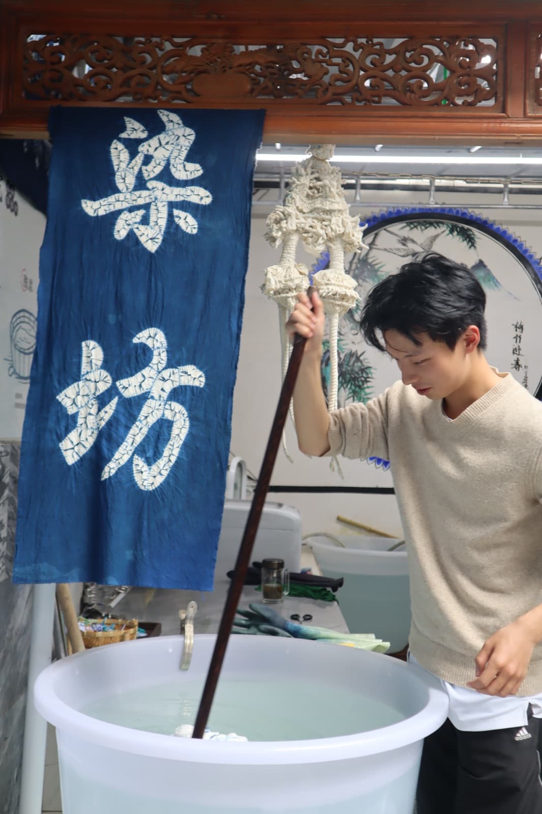A young dyer stirring cloth into an indigo vat beneath a hanging dye-house banner
