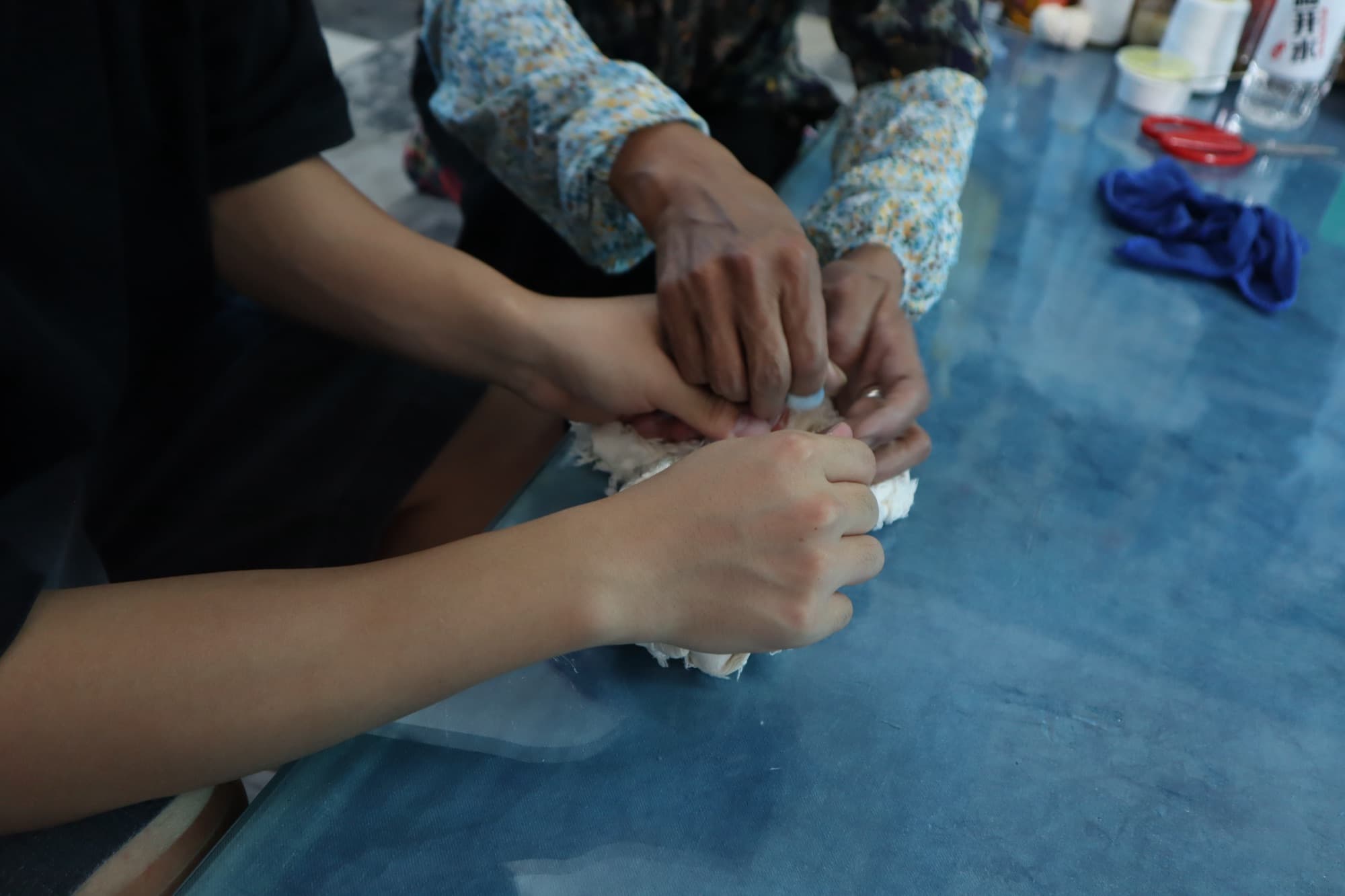 The grandmother's hands guiding a younger pair through a tying knot.