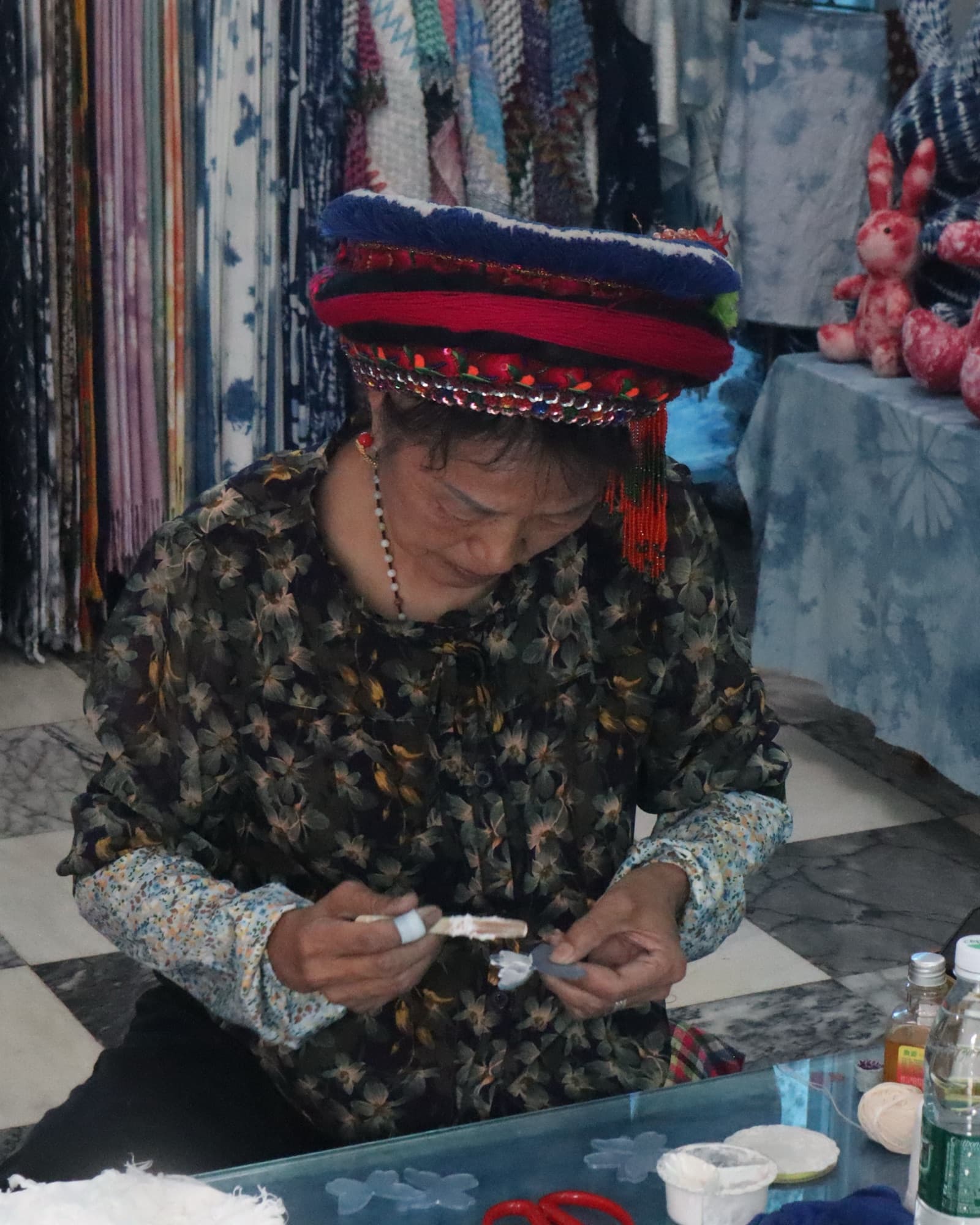 The grandmother in her Bai headdress, stitching a resist pattern at her worktable