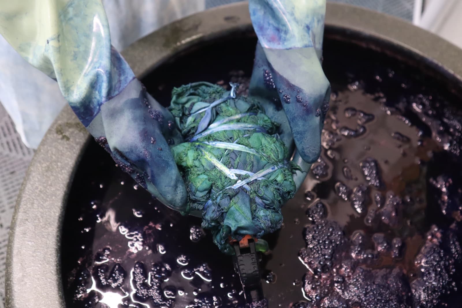 Gloved hands lowering a tied bundle into the indigo vat