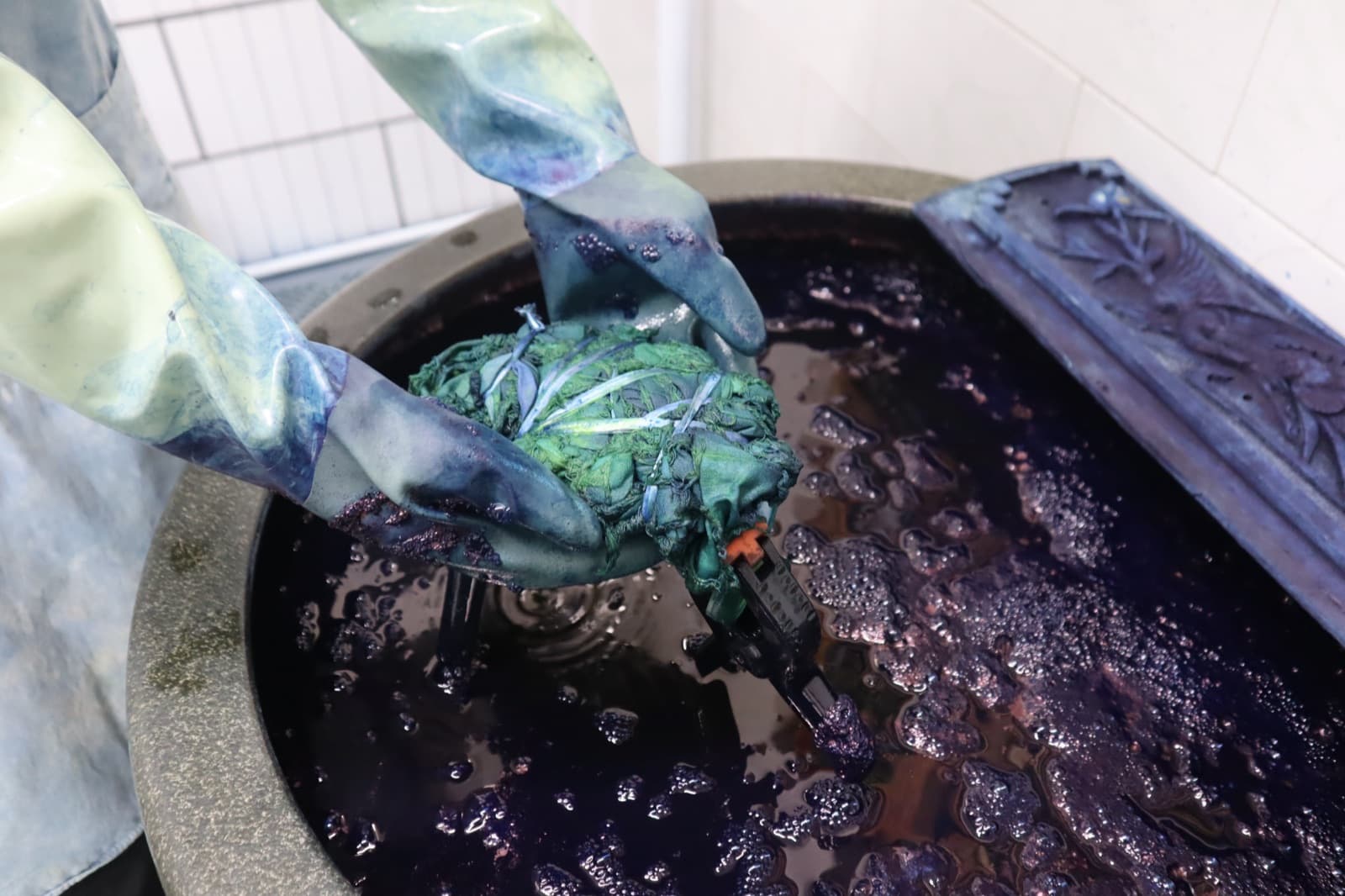 A tied bundle of cloth emerging green from the indigo vat.